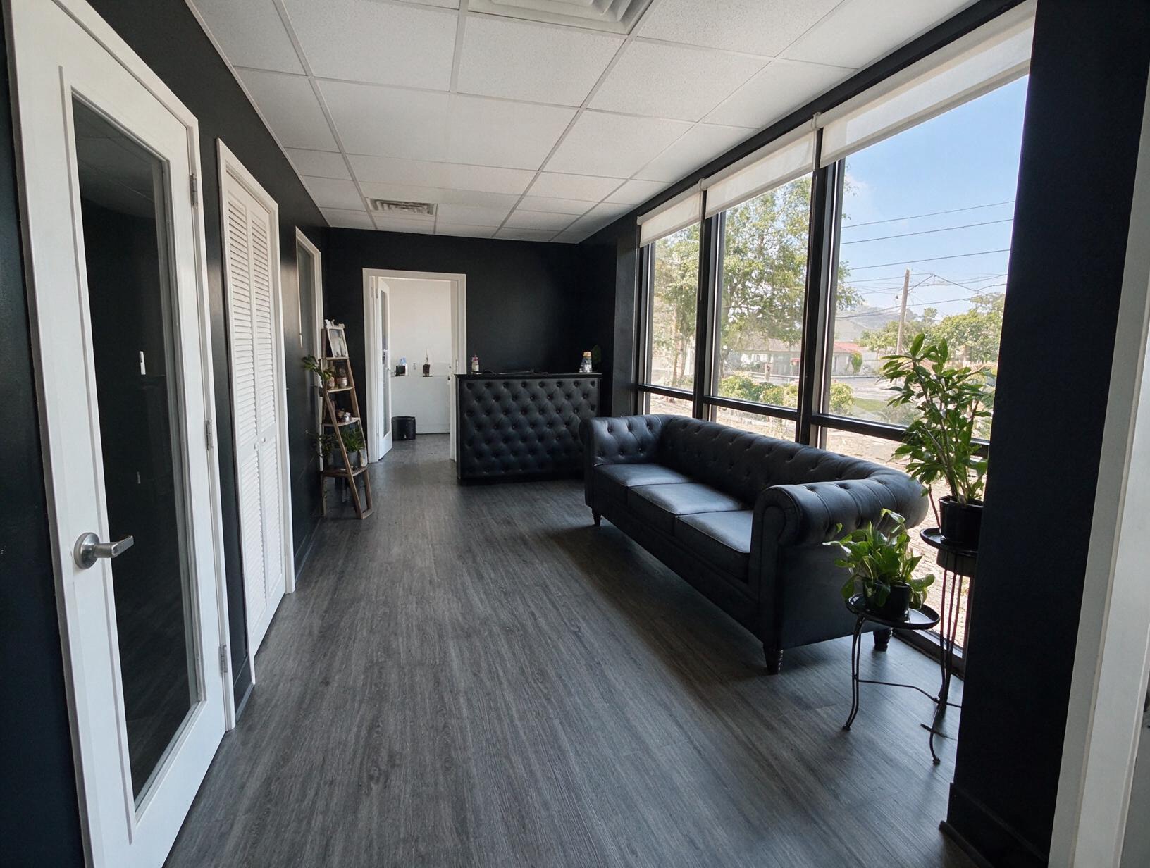 Empty dark-walled hallway with a black tufted sofa, reception desk