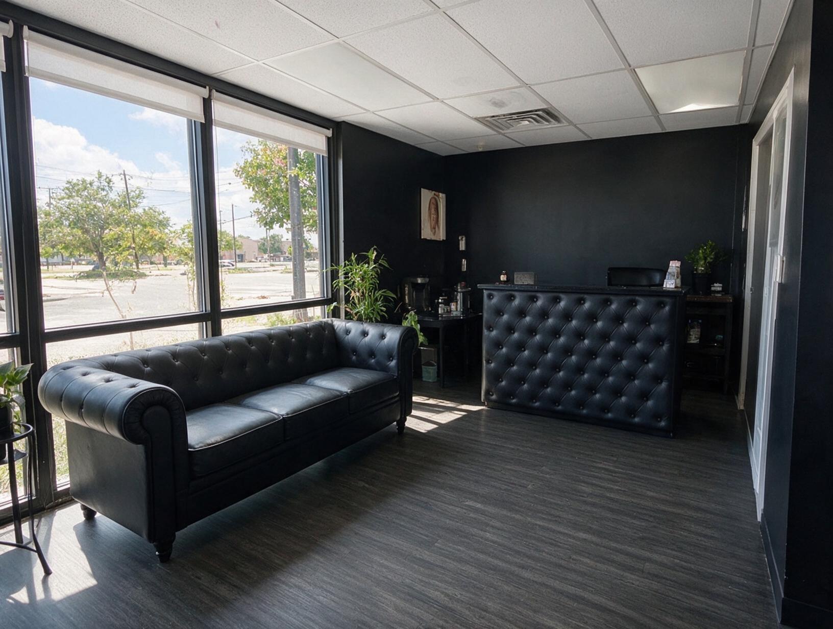 Empty reception area with black walls, a black tufted leather sofa by large windows